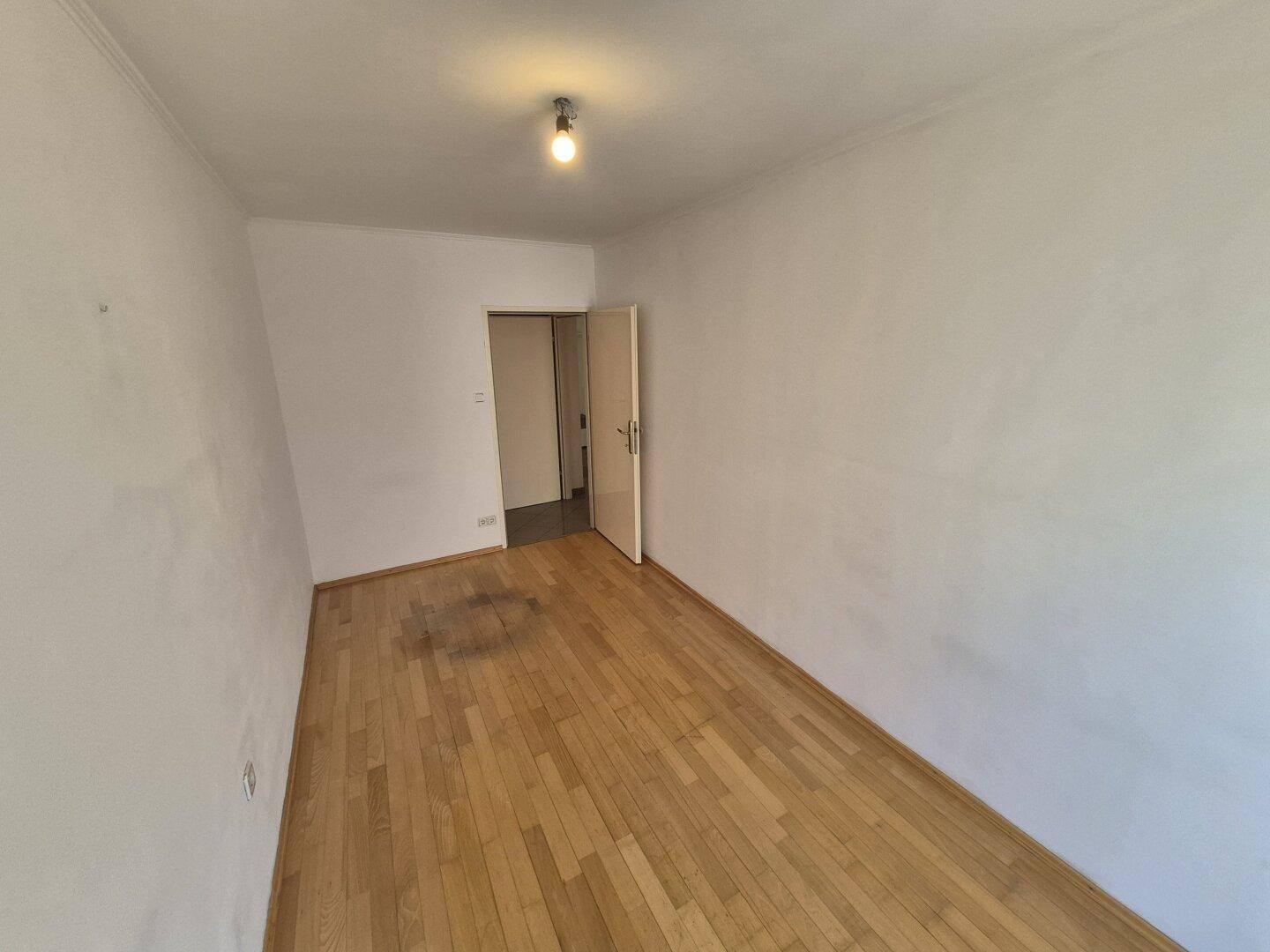 Schlafzimmer mit Parkettboden und weiß gestrichenen Wänden, ideal für persönliche Einrichtung.