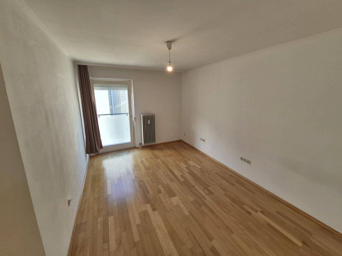 Helles Schlafzimmer mit Parkettboden und Fenster mit Vorhängen, das viel Tageslicht bietet.