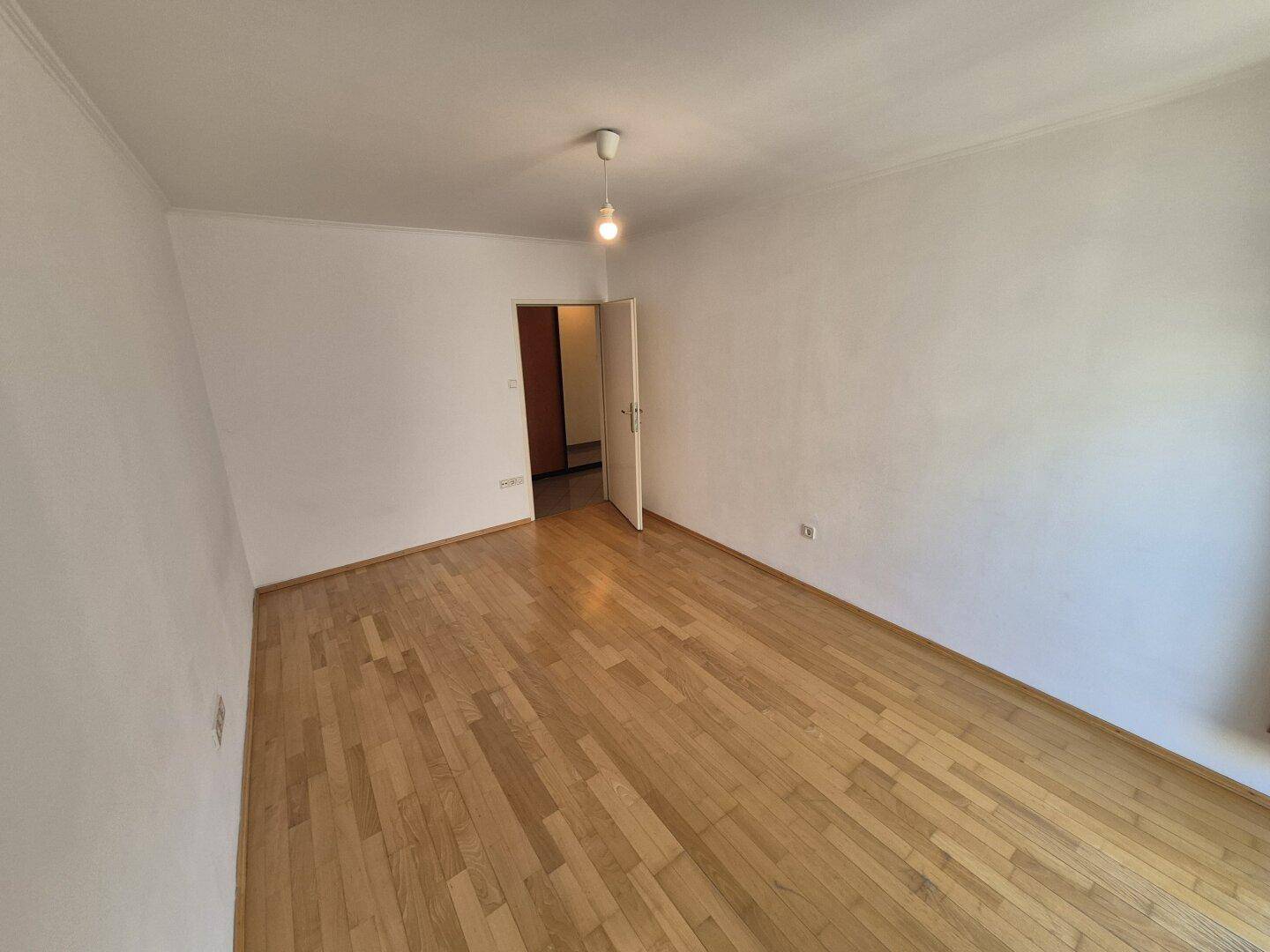 Leeres Zimmer mit hellem Parkettboden und weißen Wänden, bereit zur individuellen Gestaltung.