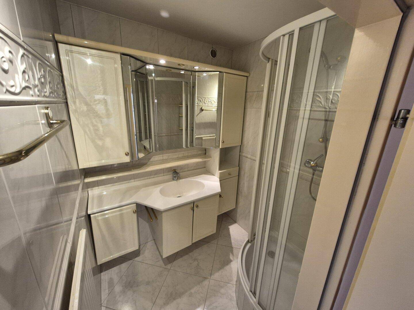 Funktionales Badezimmer mit Waschtisch, Spiegelschrank und einer Eckdusche, hell gefliest.