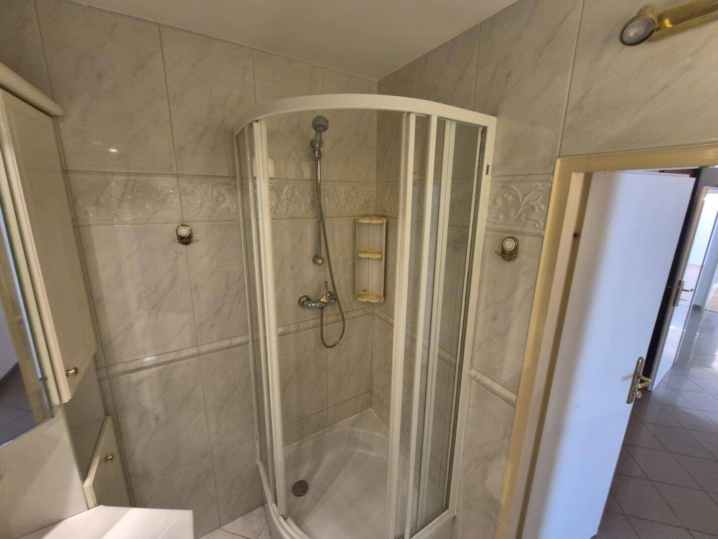 Nahaufnahme der Eckdusche im Badezimmer mit hellen Fliesen und Duscharmatur.