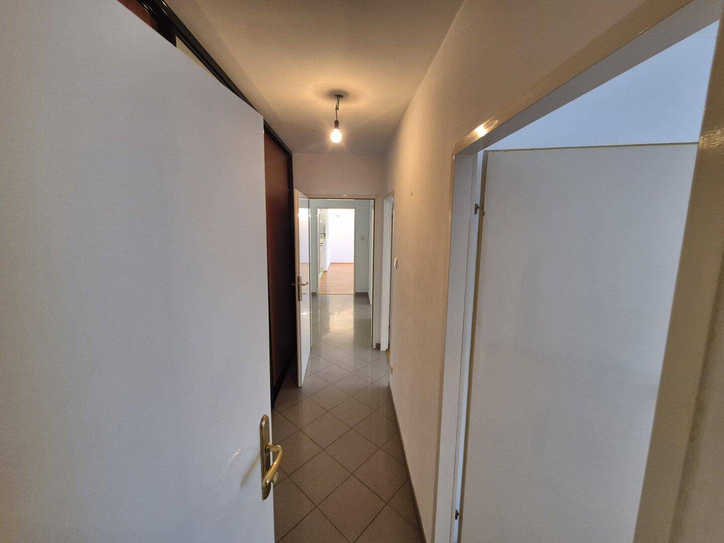 Langer, gefliester Flur mit Türen, die zu den verschiedenen Zimmern der Wohnung führen.