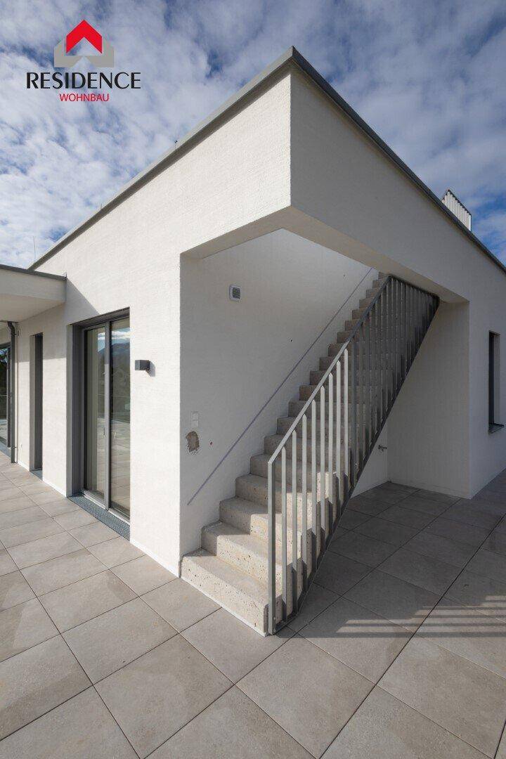 Moderne Außentreppe führt von der gefliesten Terrasse zu einer weiteren Ebene des Gebäudes.