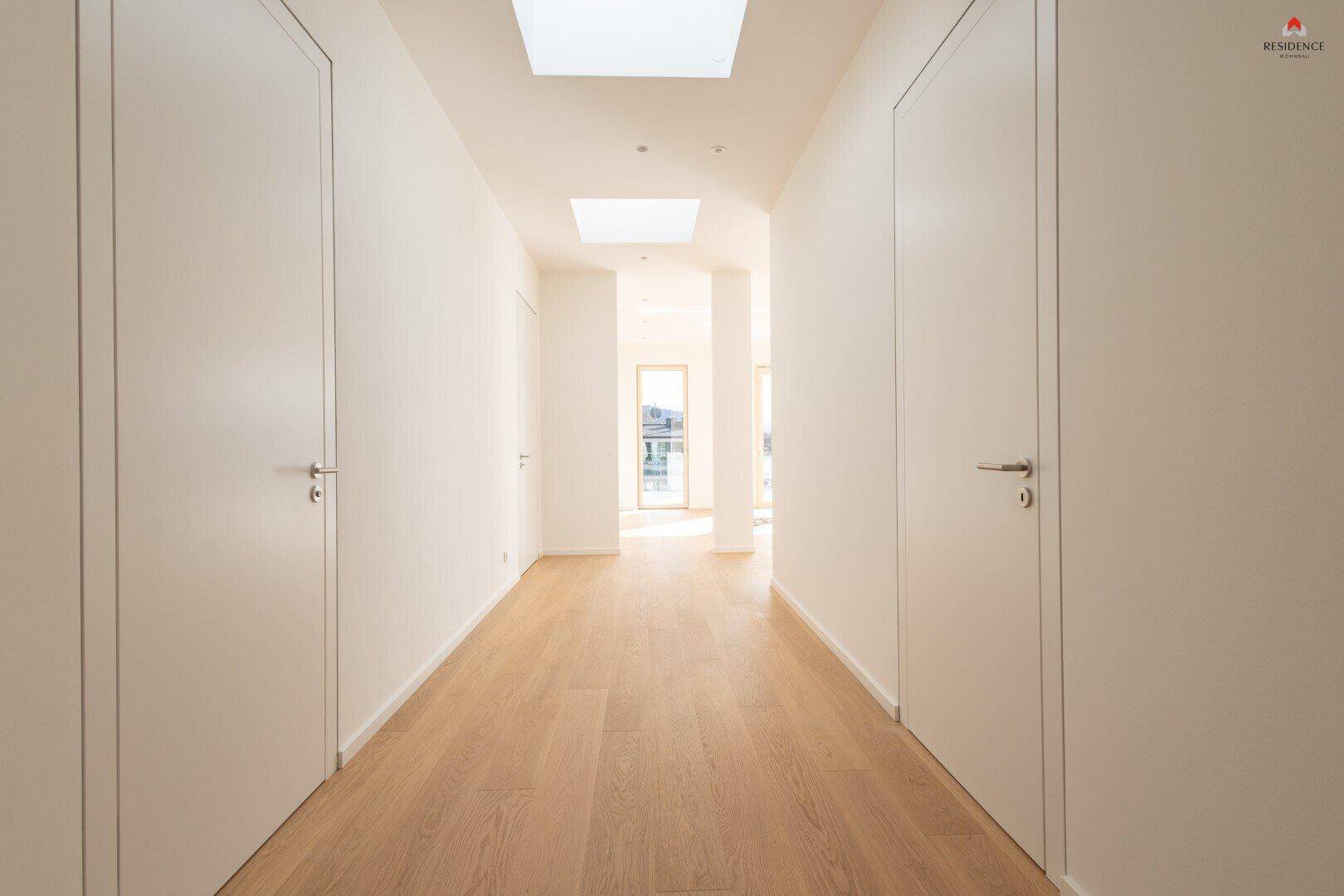 Langer, heller Flur mit Holzboden und mehreren Türen, beleuchtet durch Oberlichter in der Decke.