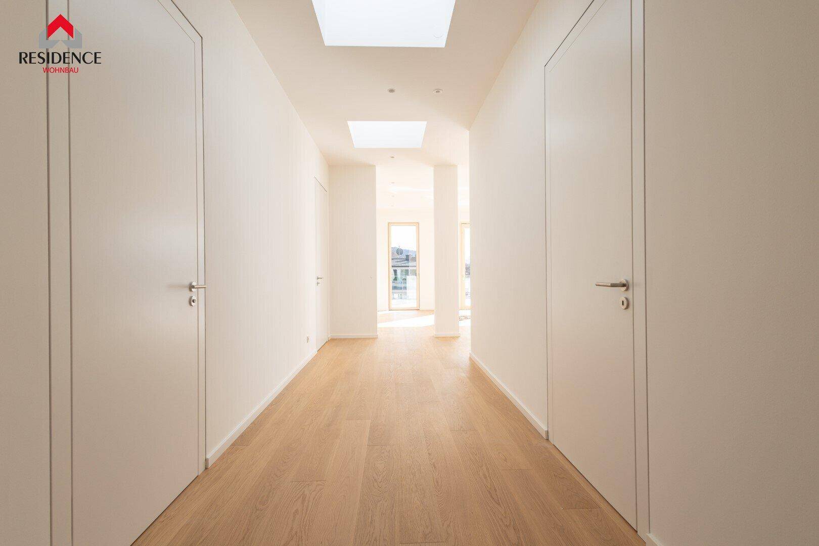 Heller Flur mit Holzboden, weißen Wänden und natürlichen Lichtquellen durch Oberlichter.