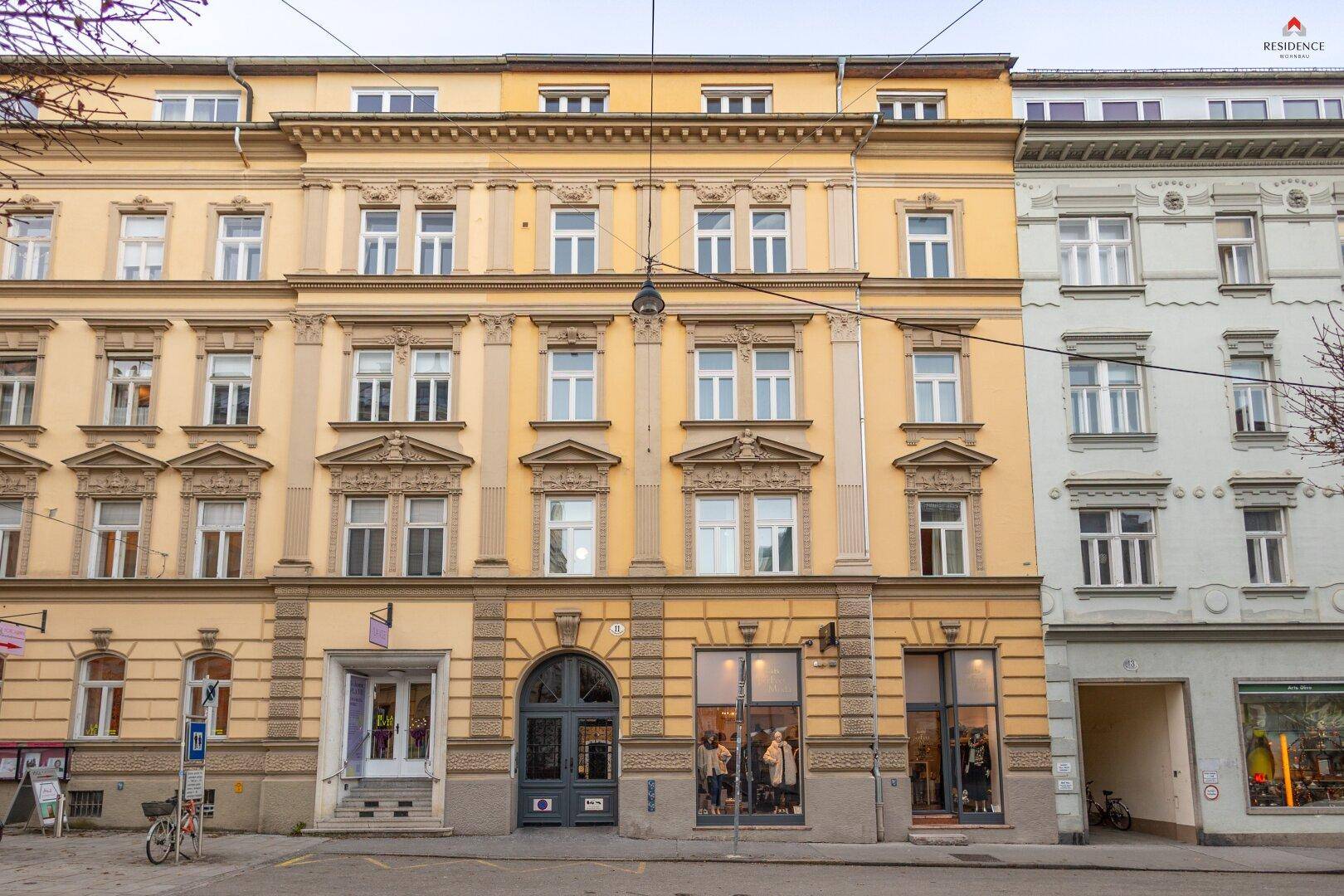 Historische Fassade eines Mehrfamilienhauses mit Geschäften im Erdgeschoss in einer städtischen Umgebung.