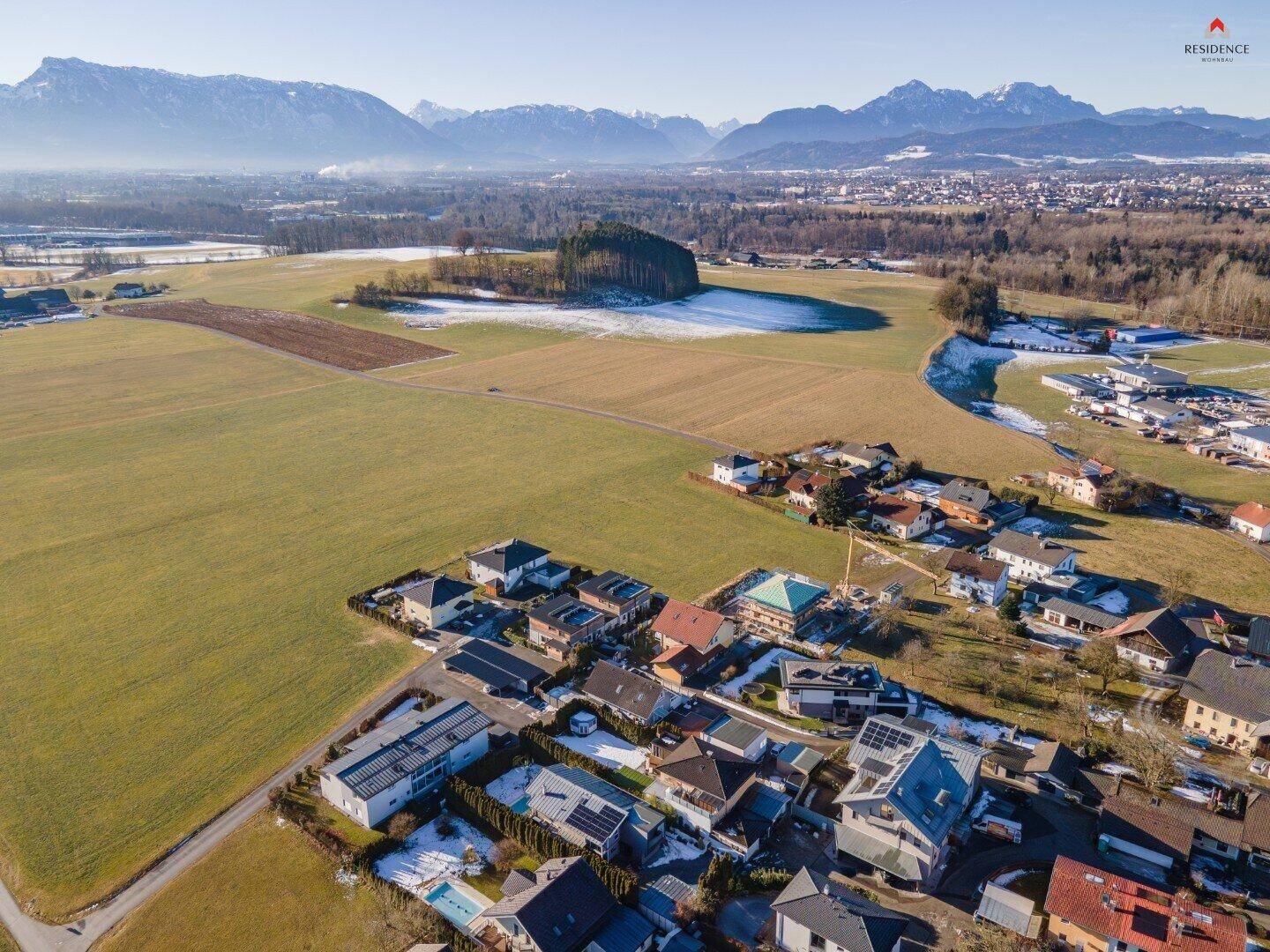 Luftaufnahme der Wohnsiedlung mit Feldern und majestätischen Bergen im Hintergrund.