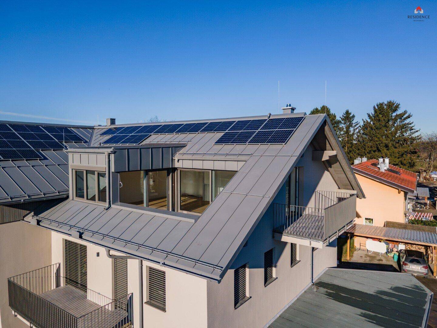 Dachansicht des Gebäudes mit Photovoltaikanlage, Gaubenfenstern und modernen Balkonen.