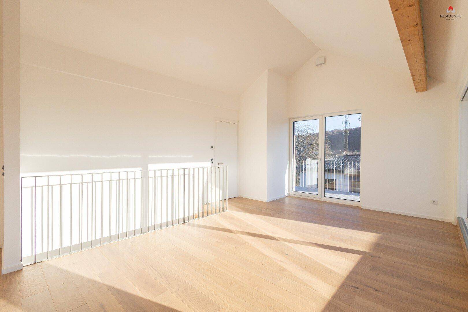 Lichtdurchfluteter offener Raum mit Parkettboden, Geländer und Zugang zu einem kleinen Balkon.