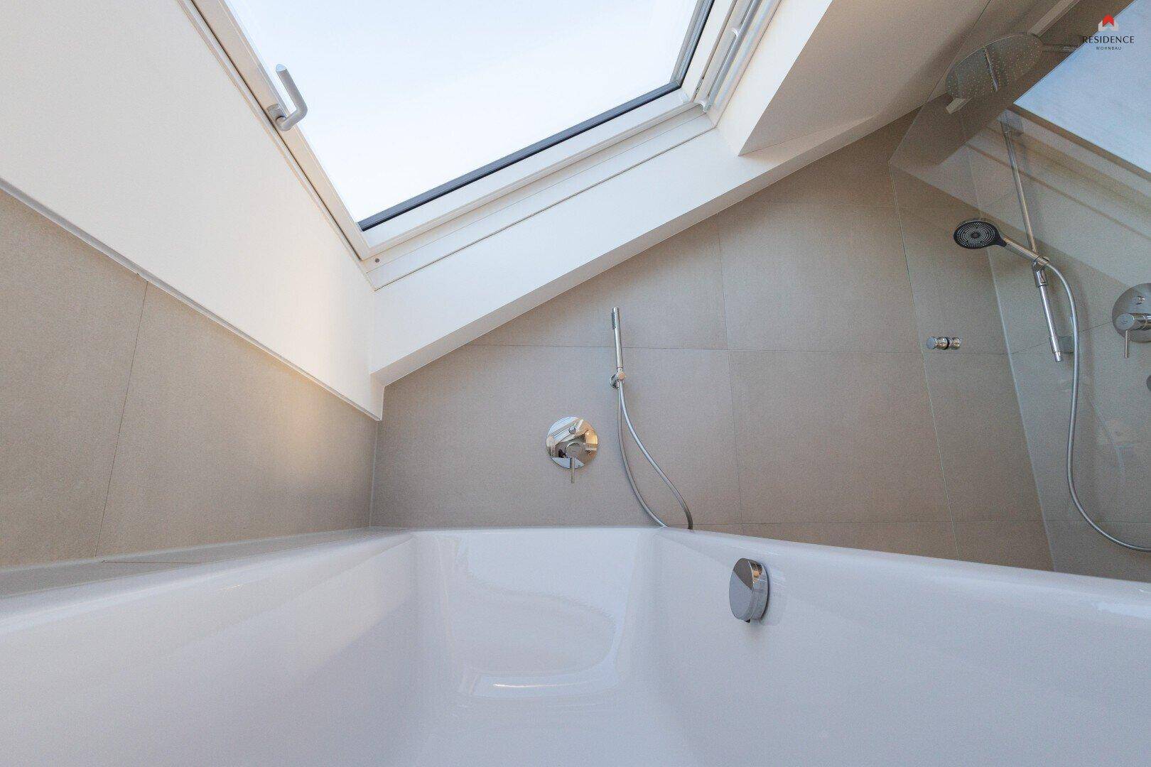 Nahaufnahme der Badewanne und Dusche im modernen Badezimmer mit natürlichem Licht durch das Dachfenster.