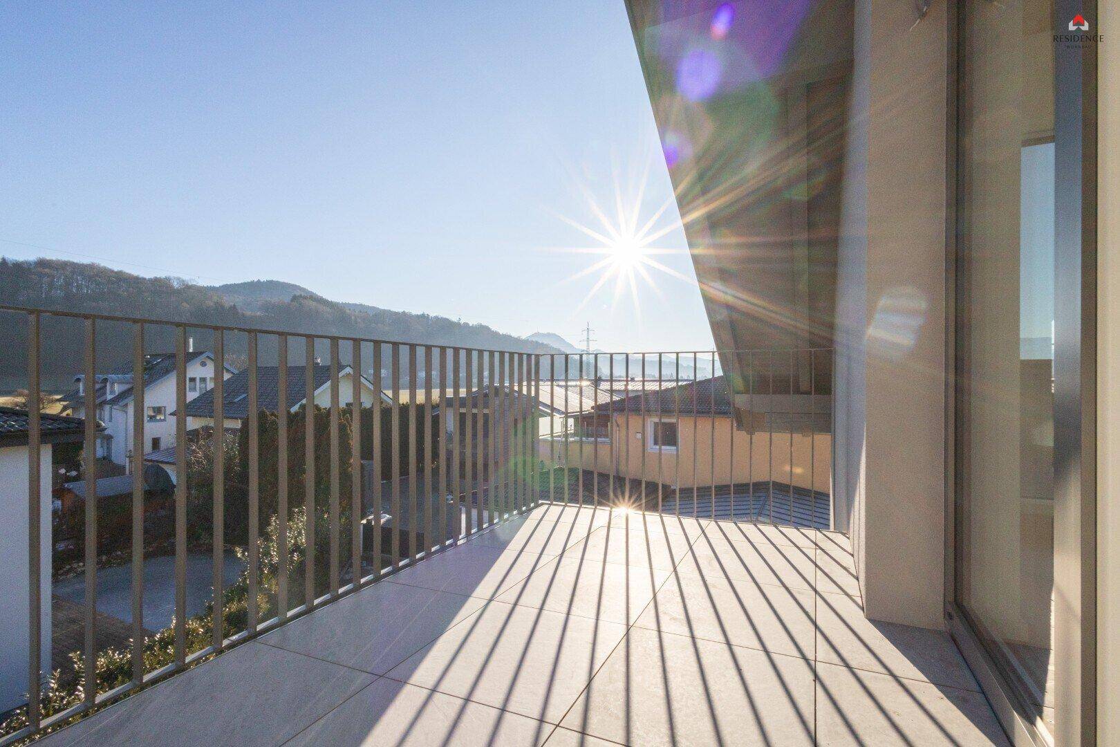 Sonniger Balkon mit Fliesenboden, Metallgeländer und weitem Blick auf die Berge.