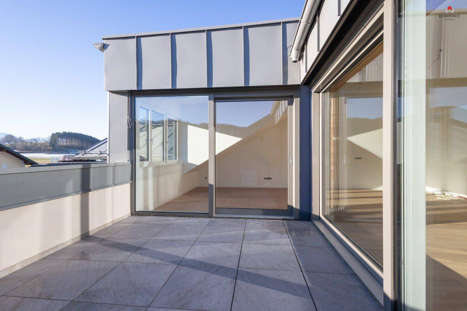 Geräumige Dachterrasse mit Fliesenboden und weitem Blick auf die umliegende Landschaft und den See.
