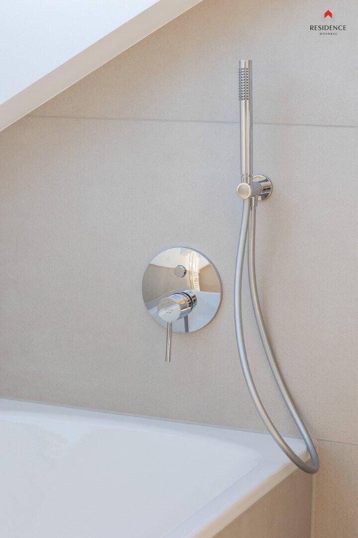 Detailaufnahme der modernen Duscharmatur und Handbrause über der Badewanne.