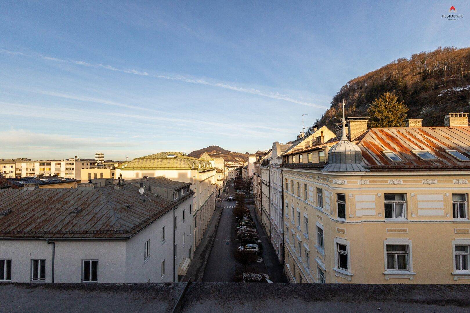 Panoramablick über die Dächer der Stadt mit Bergen im Hintergrund unter einem klaren Himmel.