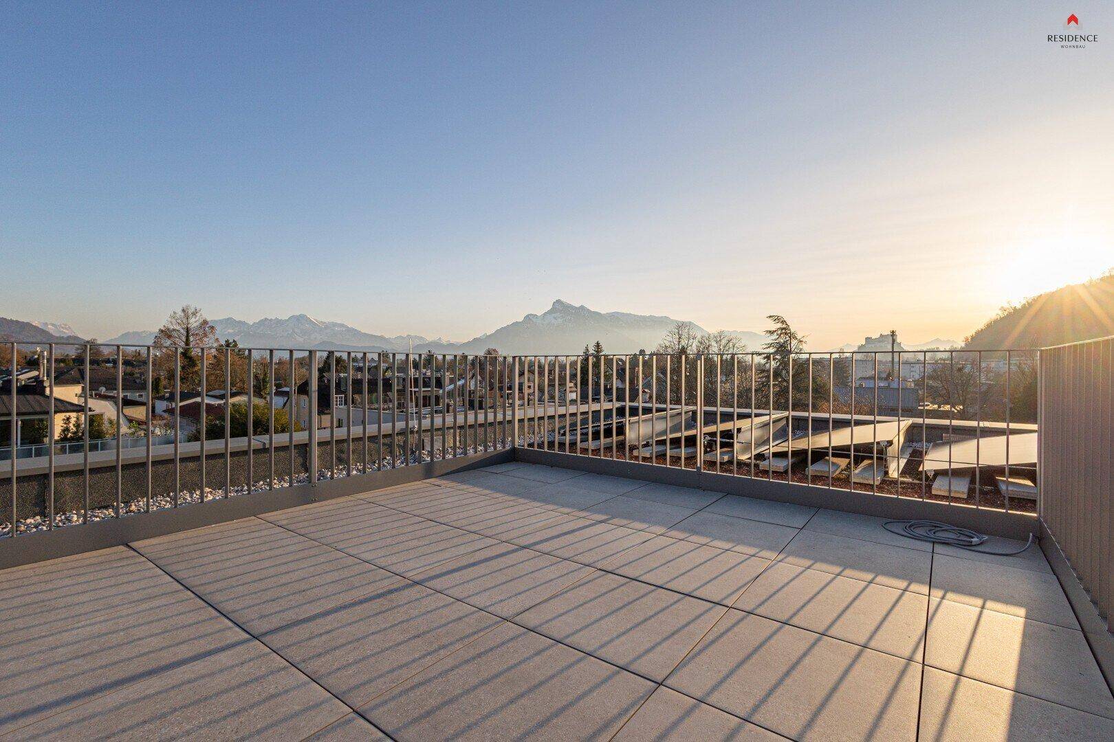 Große, leere Dachterrasse mit Metallgeländer und einem atemberaubenden Panoramablick auf die Berge bei Sonnenuntergang.