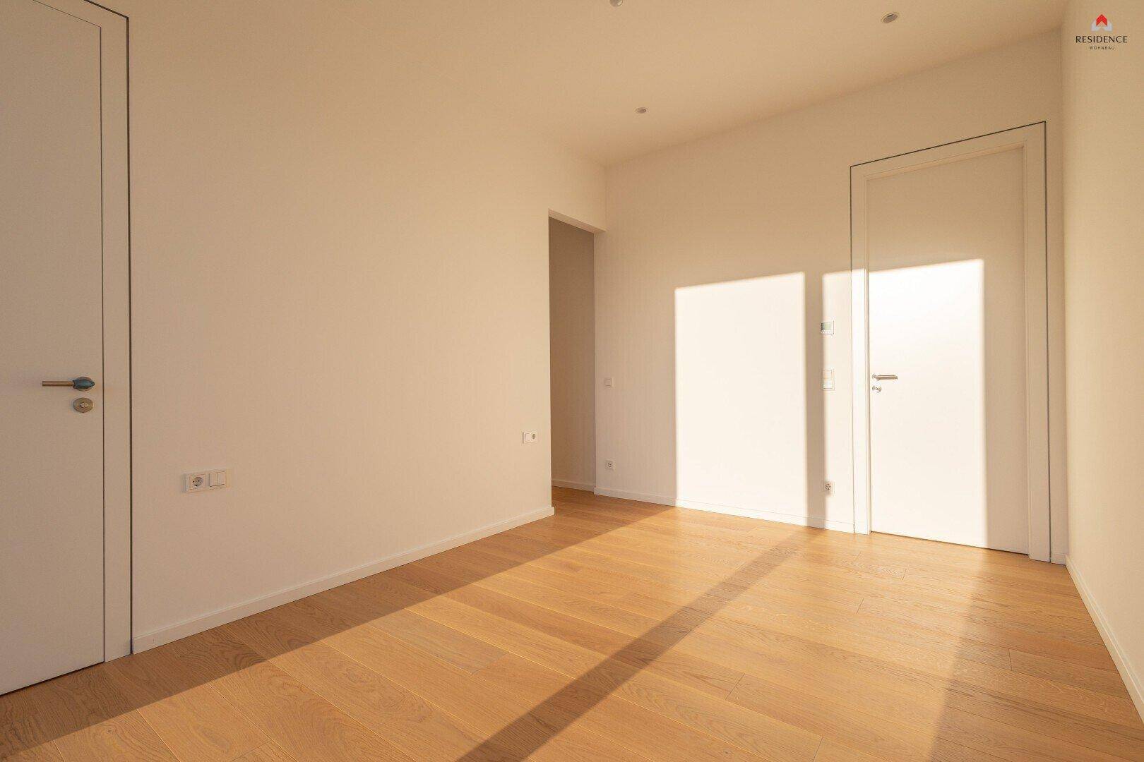 Helles, leeres Zimmer mit Holzboden und weißen Wänden, ideal als Schlaf- oder Arbeitszimmer.