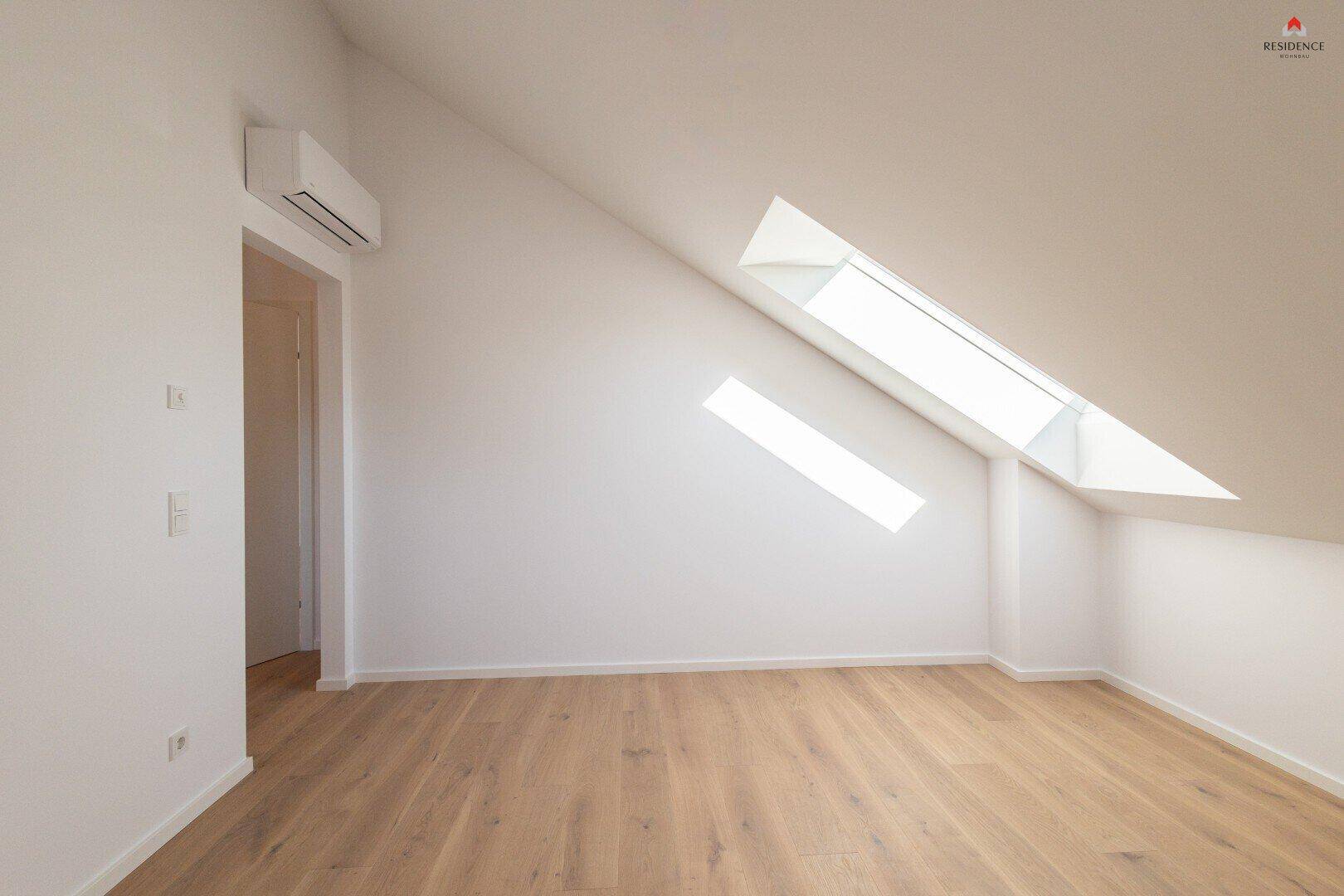 Helles Schlafzimmer im Dachgeschoss mit Holzboden, Dachschrägen und zwei Dachfenstern.