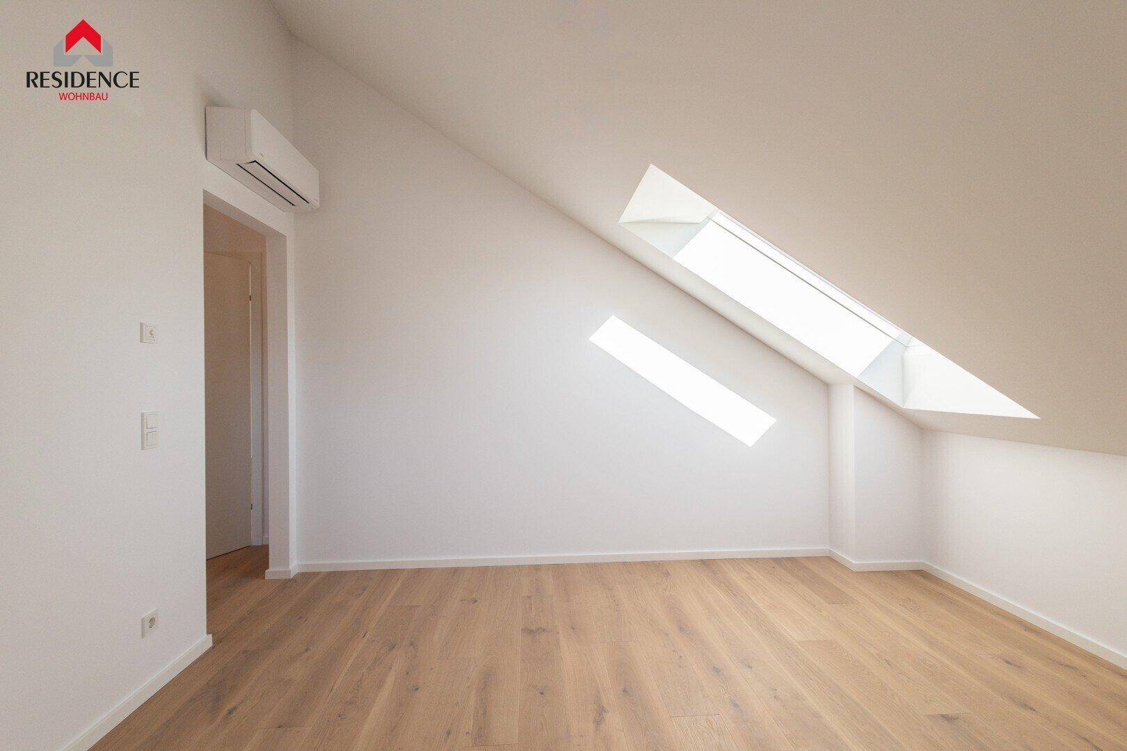 Helles Zimmer im Dachgeschoss mit Holzboden, Dachschrägen und zwei Dachfenstern.