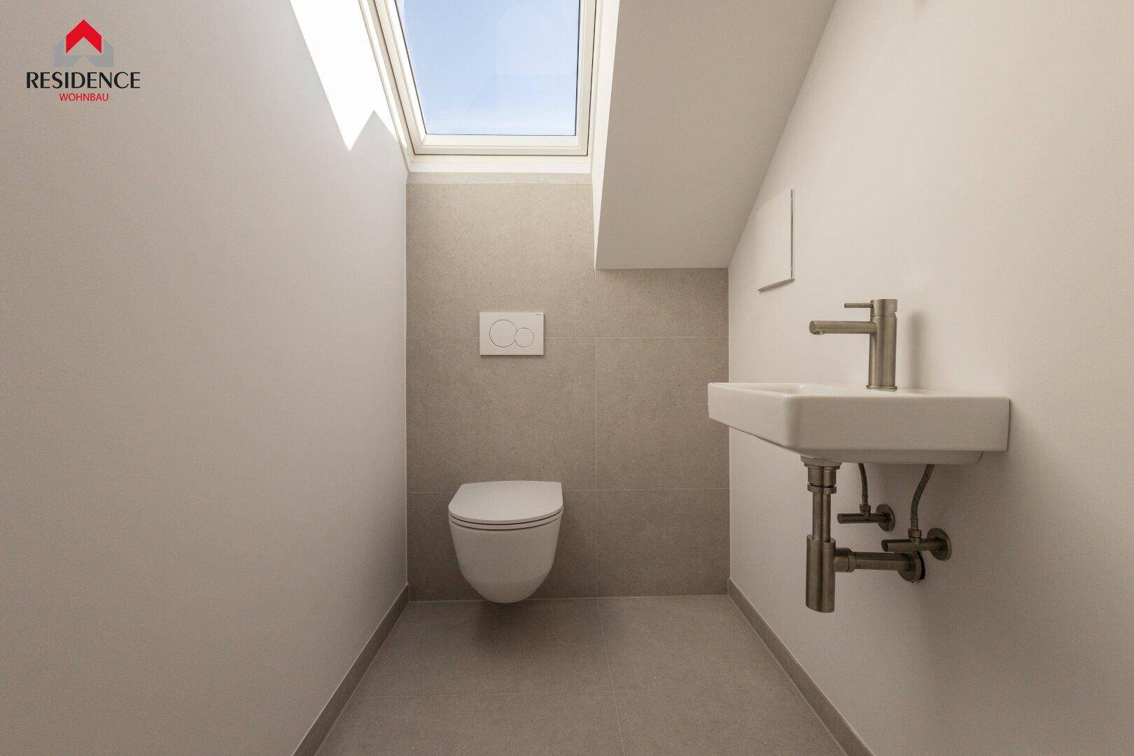 Separates Gäste-WC mit Wand-WC, kleinem Waschbecken, Fliesen und Dachfenster.