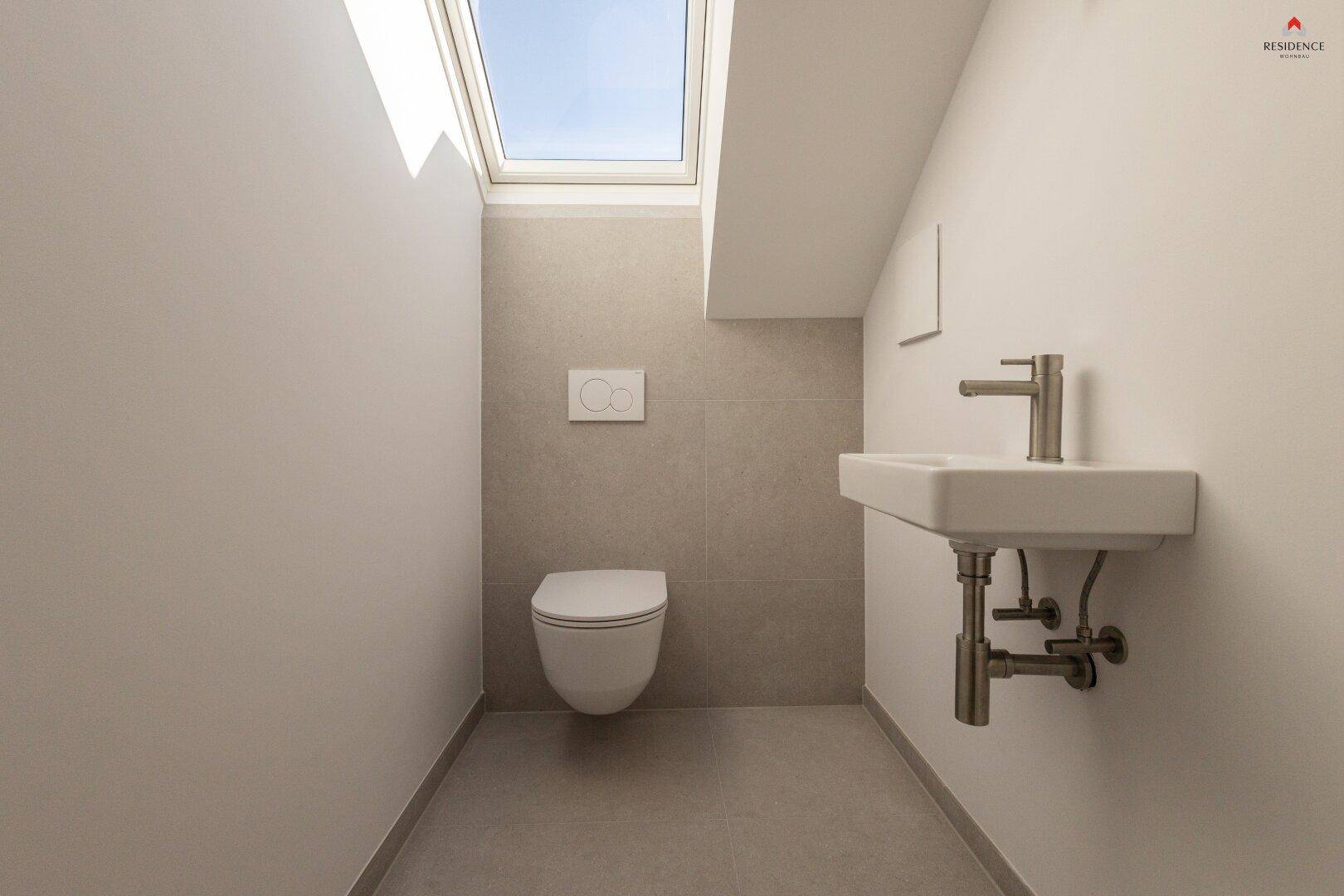 Gäste-WC mit modernem Wand-WC, kleinem Waschtisch und natürlichem Licht durch ein Dachfenster.