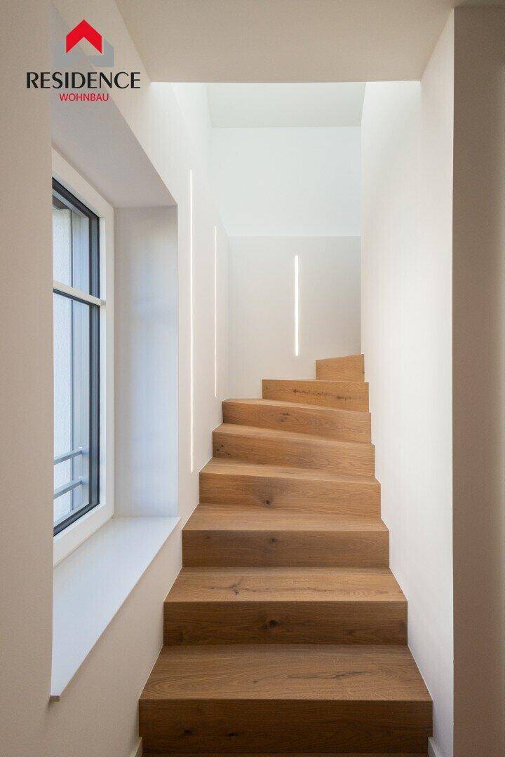 Elegante Holztreppe mit natürlichem Lichteinfall durch ein Fenster und integrierter Beleuchtung.