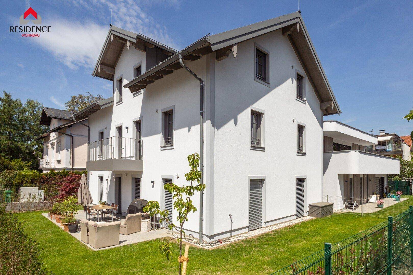 Modernes Einfamilienhaus mit weißer Fassade, Garten und Terrasse im Grünen.