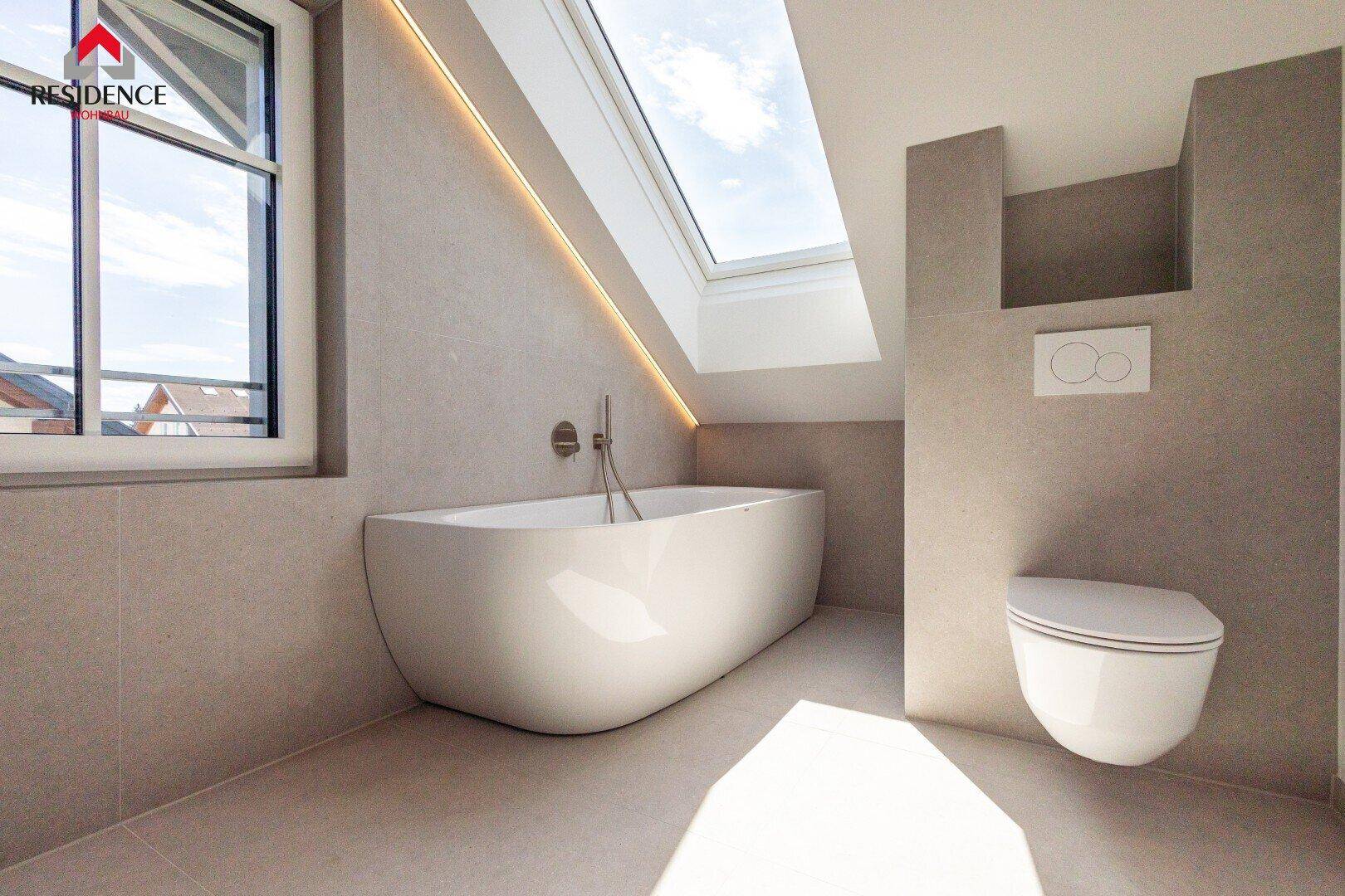 Modernes Badezimmer mit freistehender Badewanne, Wand-WC, Fliesenboden und Dachfenster.