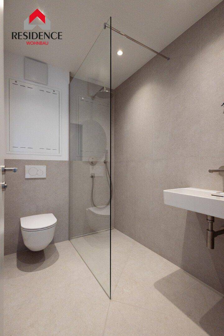 Modernes Badezimmer mit ebenerdiger Dusche, Wand-WC, Fliesenboden und minimalistischem Design.