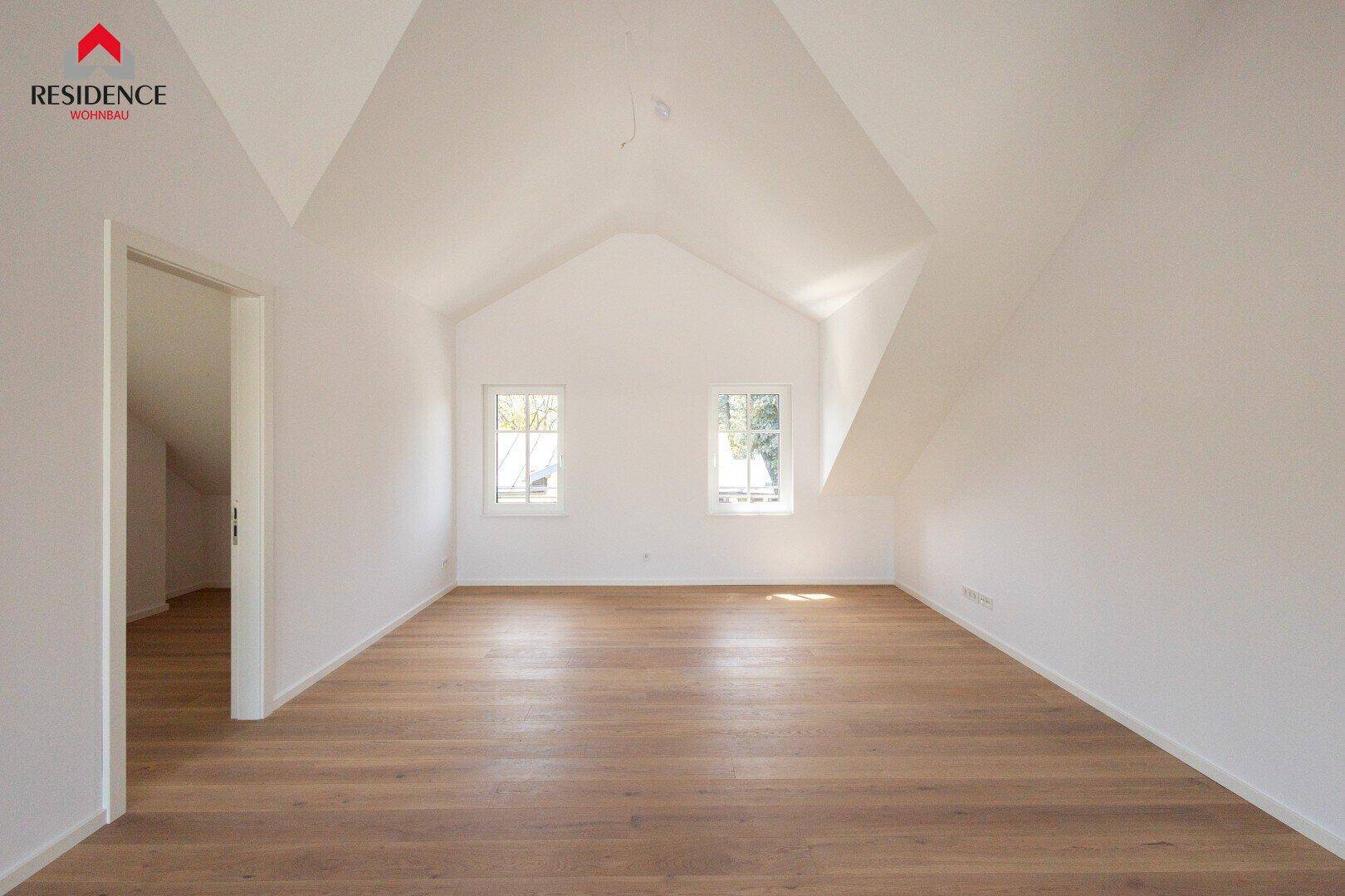 Geräumiges Schlafzimmer im Dachgeschoss mit Holzboden, hohen Decken und zwei Fenstern.