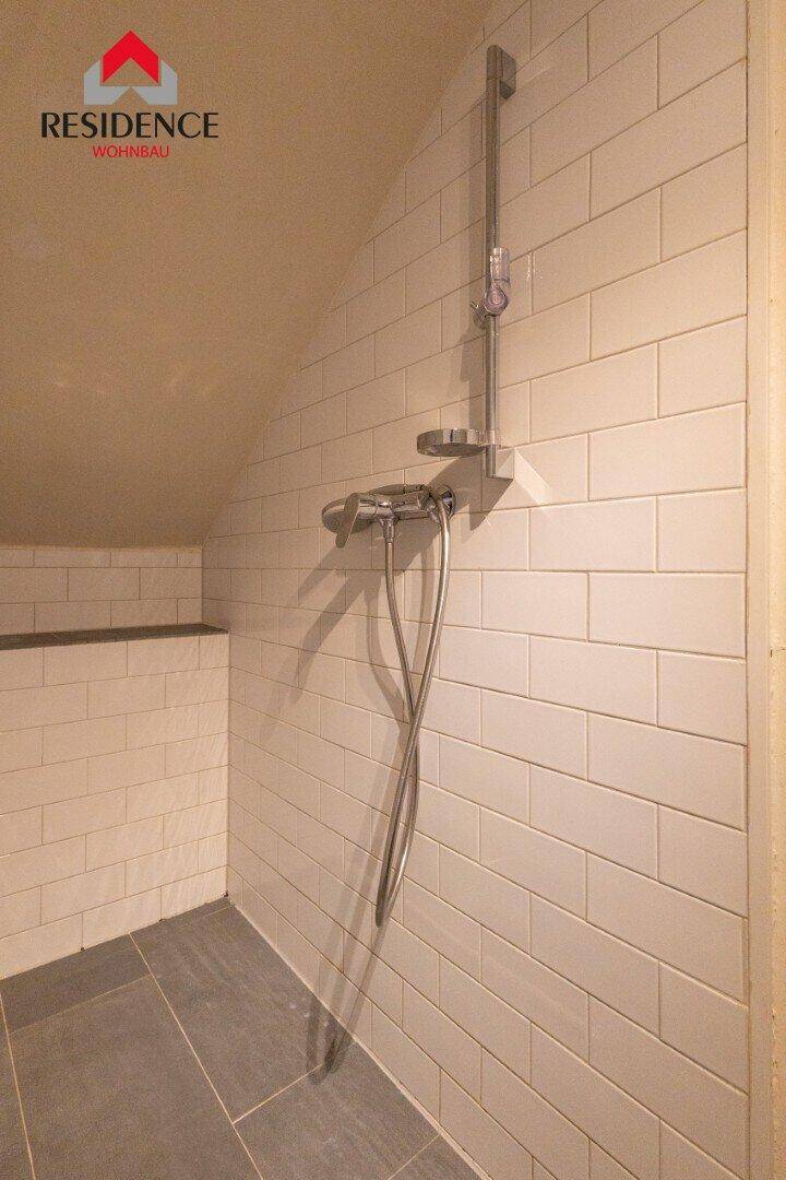 Duschbereich mit weißen Metrofliesen, moderner Armatur und dunklem Fliesenboden unter einer Dachschräge.