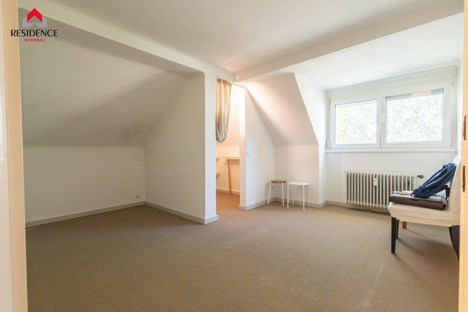 Helles Schlafzimmer mit Teppichboden, Fenster und charakteristischen Dachschrägen, unmöbliert und geräumig.