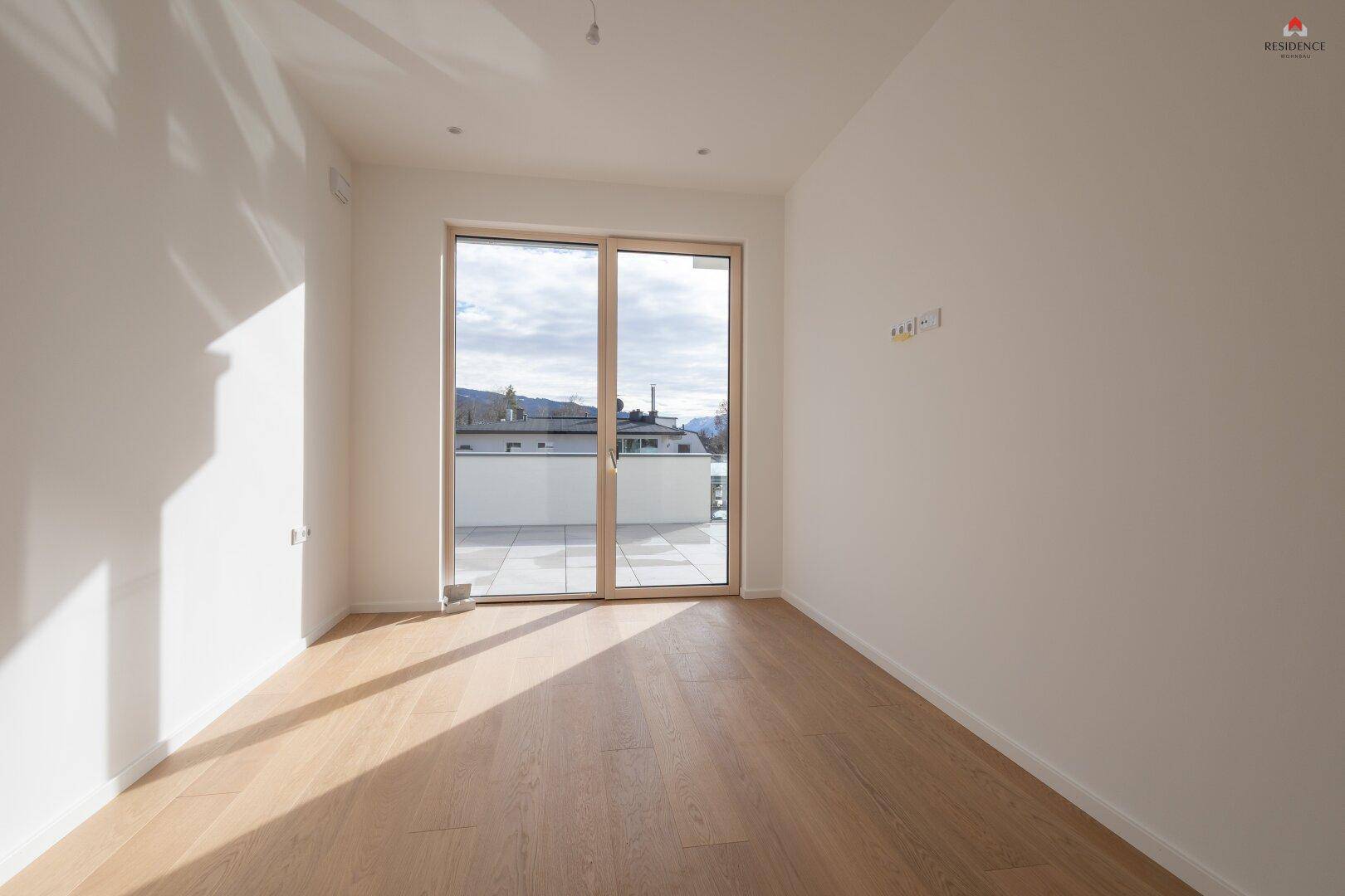 Geräumiges Zimmer mit Holzboden und Schiebetür, die Zugang zu einem Außenbereich bietet.