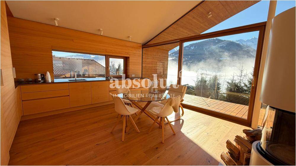Moderne Küche mit Holzelementen, Essbereich und beeindruckendem Blick auf die verschneiten Berge.