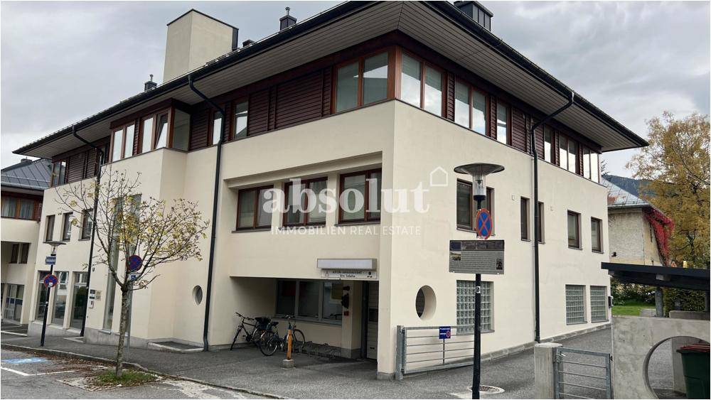Modernes Gebäude mit heller Fassade, großen Fenstern und traditionellem Dachüberstand in einer städtischen Umgebung.