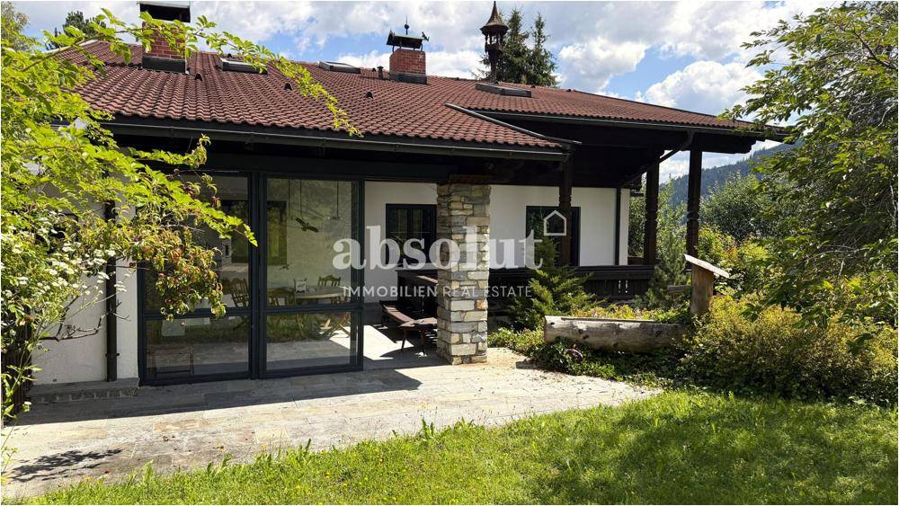 Gemütliche Terrasse vor dem Haus mit großen Glasfronten und traditionellen Steinelementen.