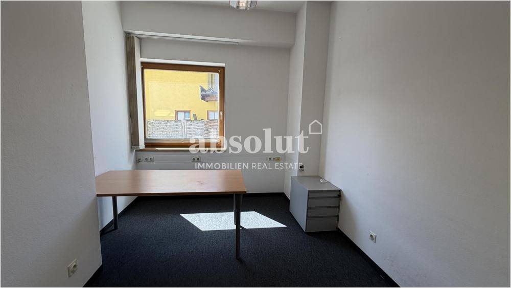 Kleineres Büro mit einem Schreibtisch, Rollcontainer und Teppichboden.