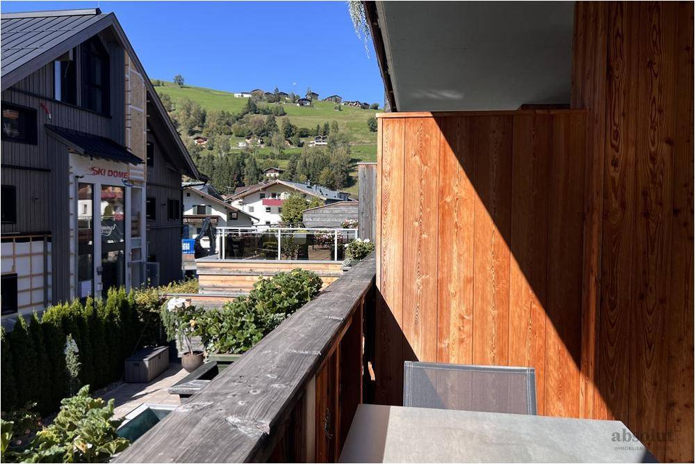 Balkon mit Holzwänden und Blick auf die umliegende Bebauung und grüne Hügel.