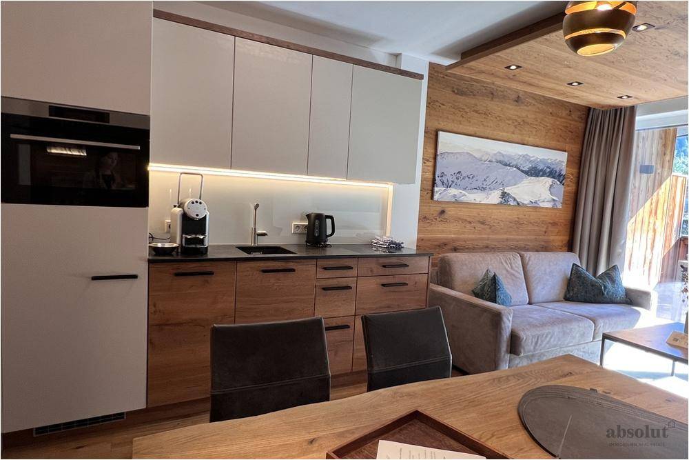 Moderne Einbauküche mit hellen Fronten, Holzdetails und hochwertigen Geräten im Wohnbereich.