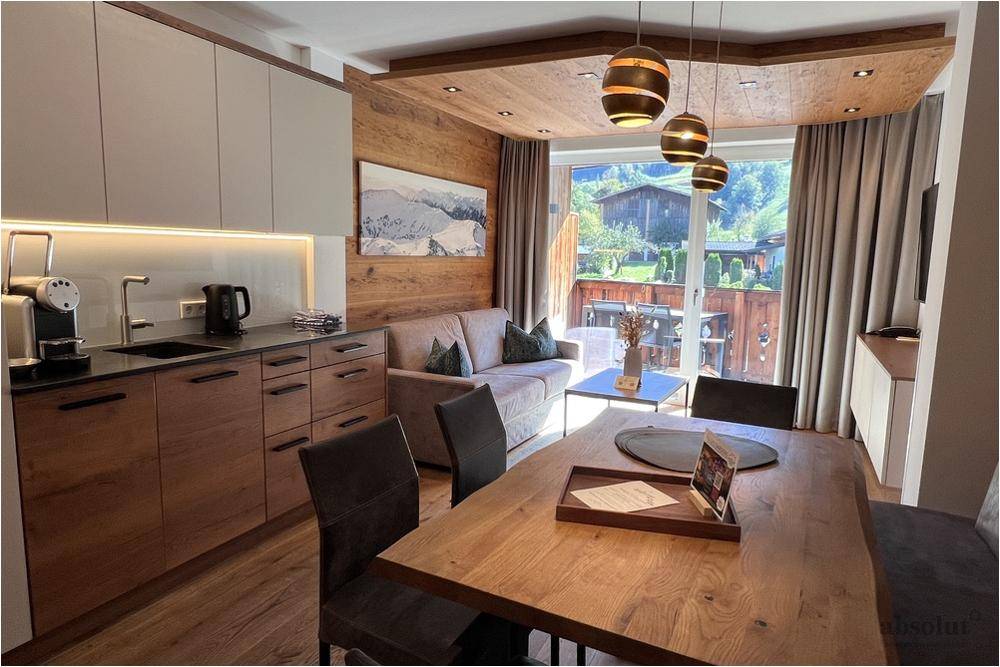 Moderner Wohn-Essbereich mit integrierter Küche und Zugang zu einem möblierten Balkon.