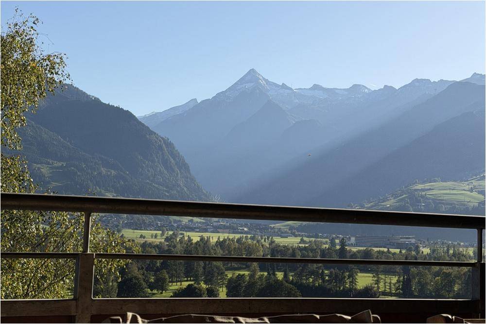 Panoramablick auf die umliegende Berglandschaft und das Tal von einem Balkon an einem sonnigen Tag.