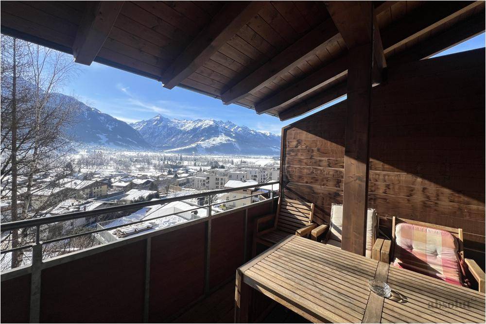 Überdachter Balkon mit Holzboden, Sitzgelegenheiten und weitem Blick auf die verschneite Bergwelt.
