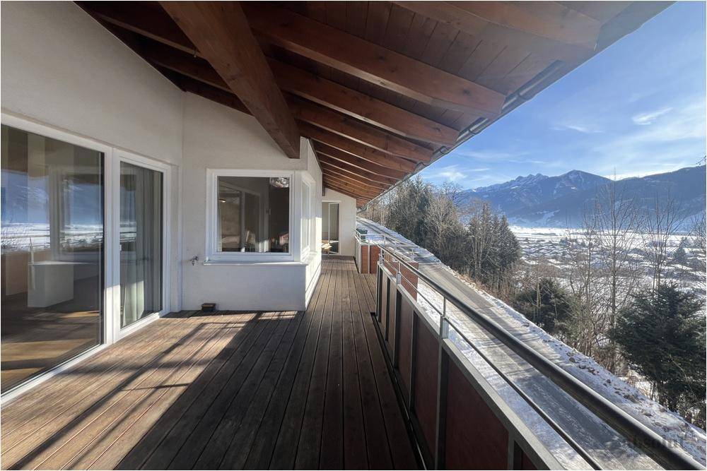 Langer Holzbalkon mit Panoramablick auf die verschneite Landschaft und die Berge an einem sonnigen Tag.
