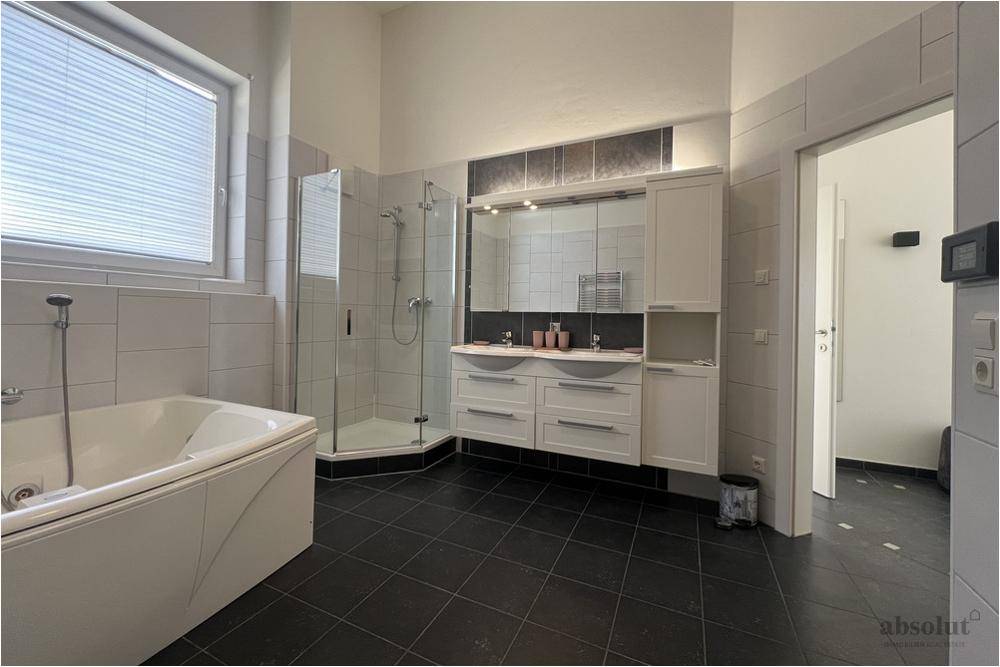 Geräumiges Badezimmer mit Eckbadewanne, Dusche, Doppelwaschbecken, Spiegelschrank und Fenster.