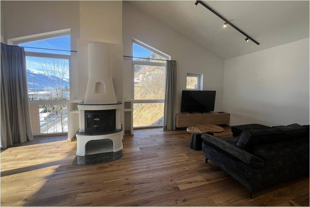 Helles Wohnzimmer mit modernem Kamin, Holzboden und großen Fenstern mit Bergblick im Winter.