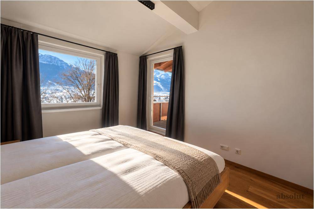 Helles Schlafzimmer mit Holzboden, Bergblick und Zugang zu einem kleinen Balkon im Winter.