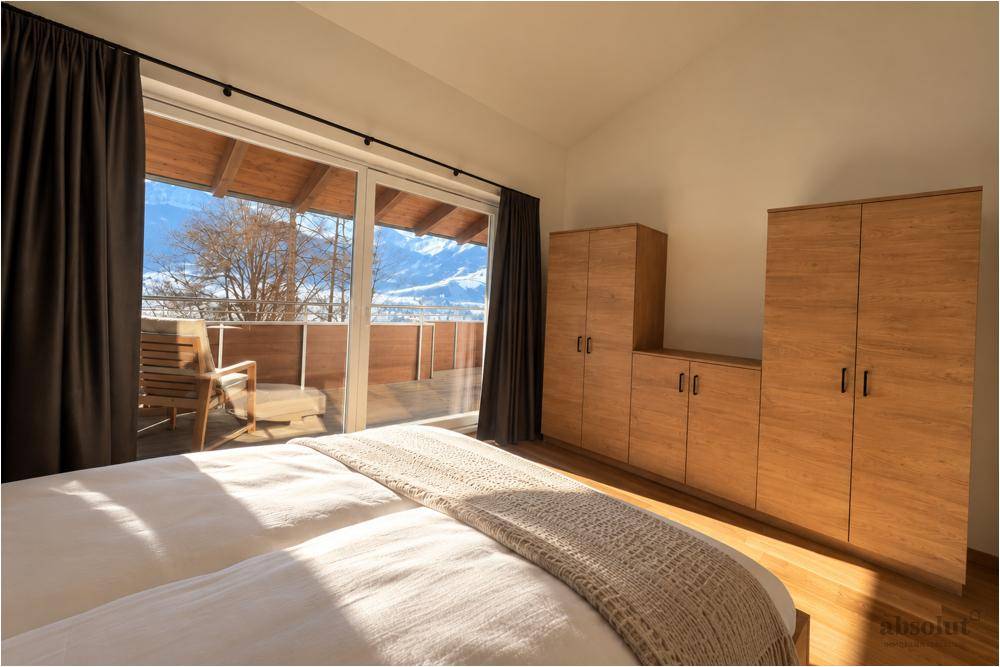 Schlafzimmer mit Holzboden, Einbauschränken und Zugang zu einem sonnigen Balkon mit Bergblick.