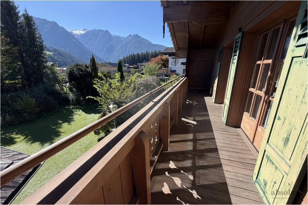 Langer Holzbalkon mit traditionellem Geländer und weitem Blick auf die umliegende Bergwelt.