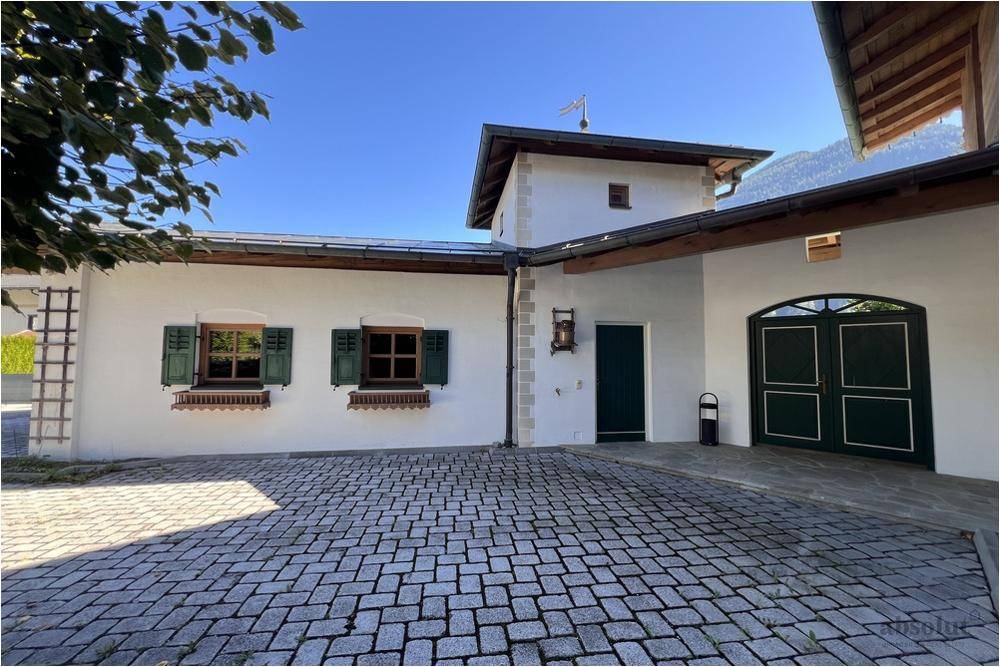 Traditionelle Hausfassade mit gepflastertem Hof, grünen Fensterläden und Holztüren im alpenländischen Stil.