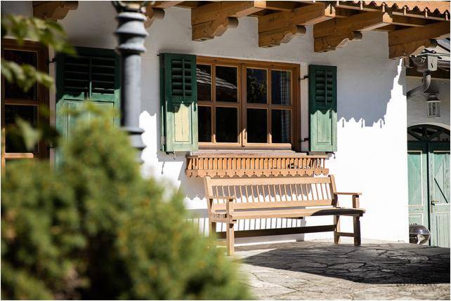Traditionelle Holzbank vor dem Haus mit grünen Fensterläden und dekorativem Fensterbrett.