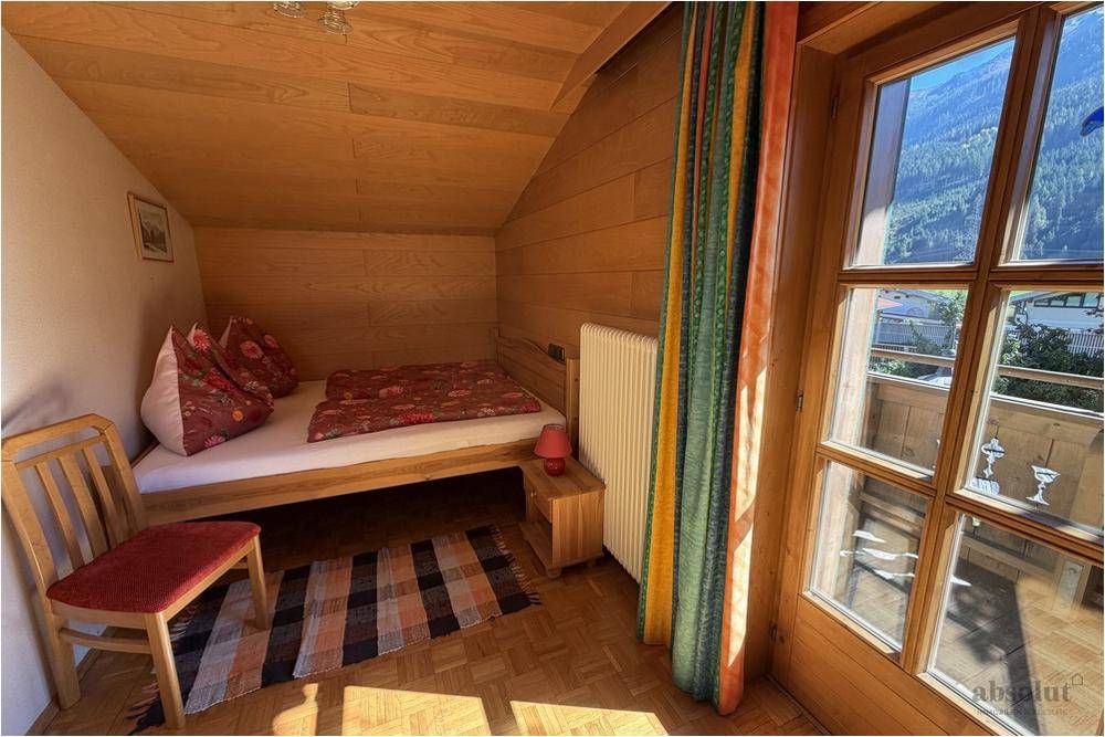 Kleines Schlafzimmer im Dachgeschoss mit Holzwänden, Einzelbett und Balkonzugang mit Bergblick.